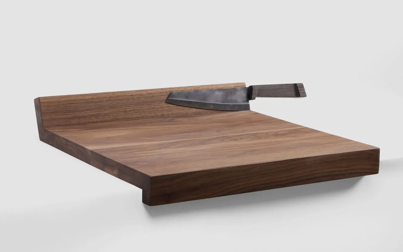 Woodsea Edge Cutting Board in walnut with a chef's knife, hooked over a kitchen counter edge
